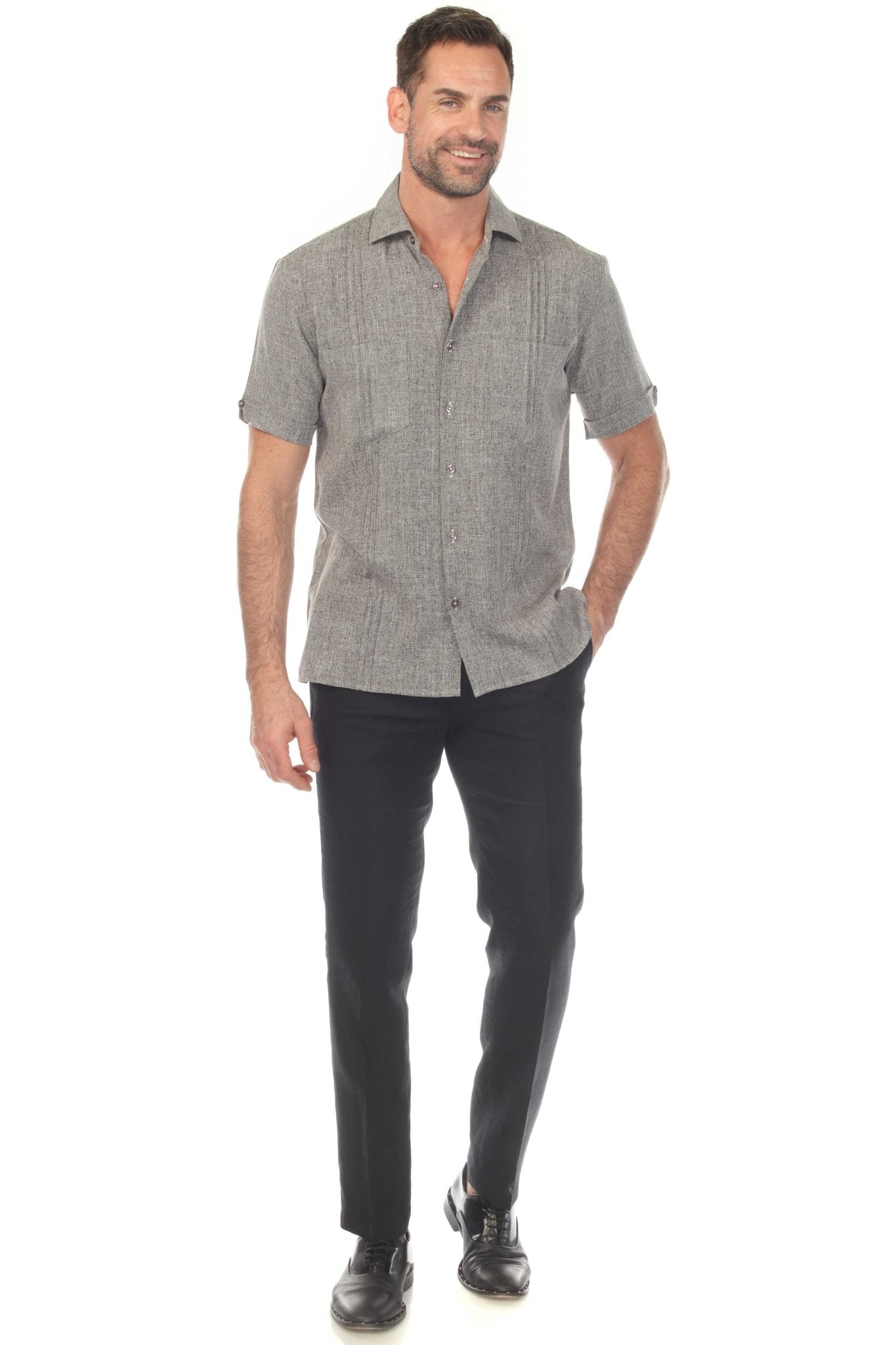 A man models a short-sleeved, gray Men’s Classic Two-Pocket Guayamisa Shirt with pleats and dark pants, facing forward.