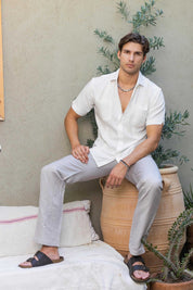 Man in a white Men’s Classic Two-Pocket Guayamisa Shirt with pleats, seated on a pot.