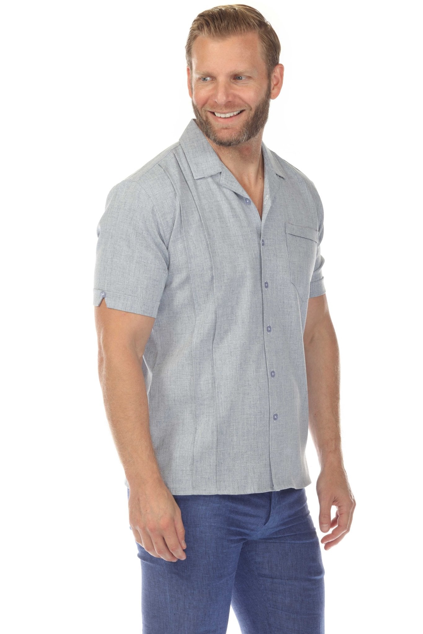 A man smiles, wearing a light blue Menâ€™s Retro Cuban Shirt with pleating and a pocket, with blue pants.