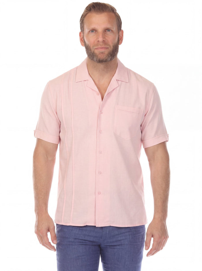 A man wears a pink Menâ€™s Retro Cuban Shirt with pleating and one pocket, holding sunglasses outside.