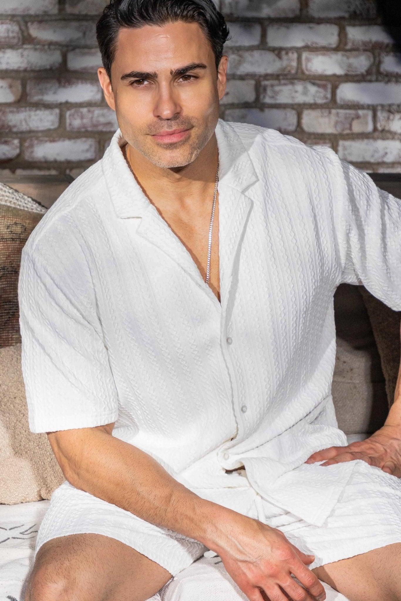 A man sits wearing the white Men's Seersucker Knit Shirt & Short Set.