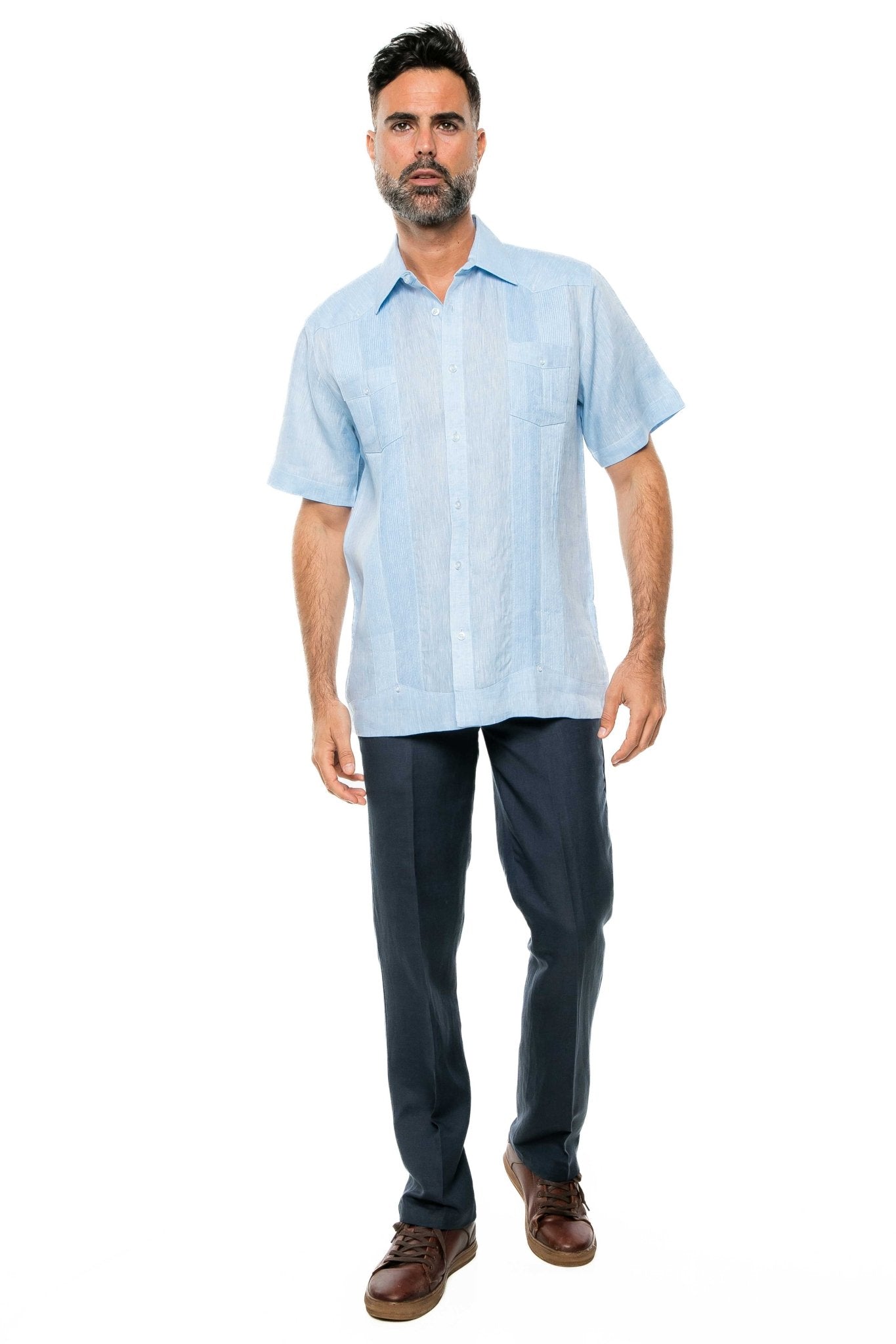 A man wears a light blue Yarn Dye 100% Linen Two Pocket Guayabera Short Sleeve shirt with dark blue trousers.