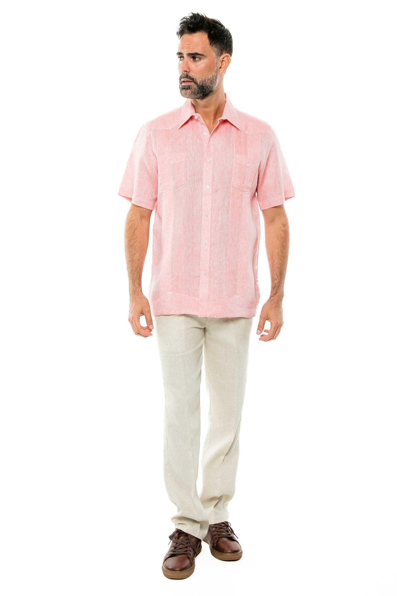 A man wears a pink Yarn Dye 100% Linen Two Pocket Guayabera short sleeve shirt with tan linen pants, against a white background.