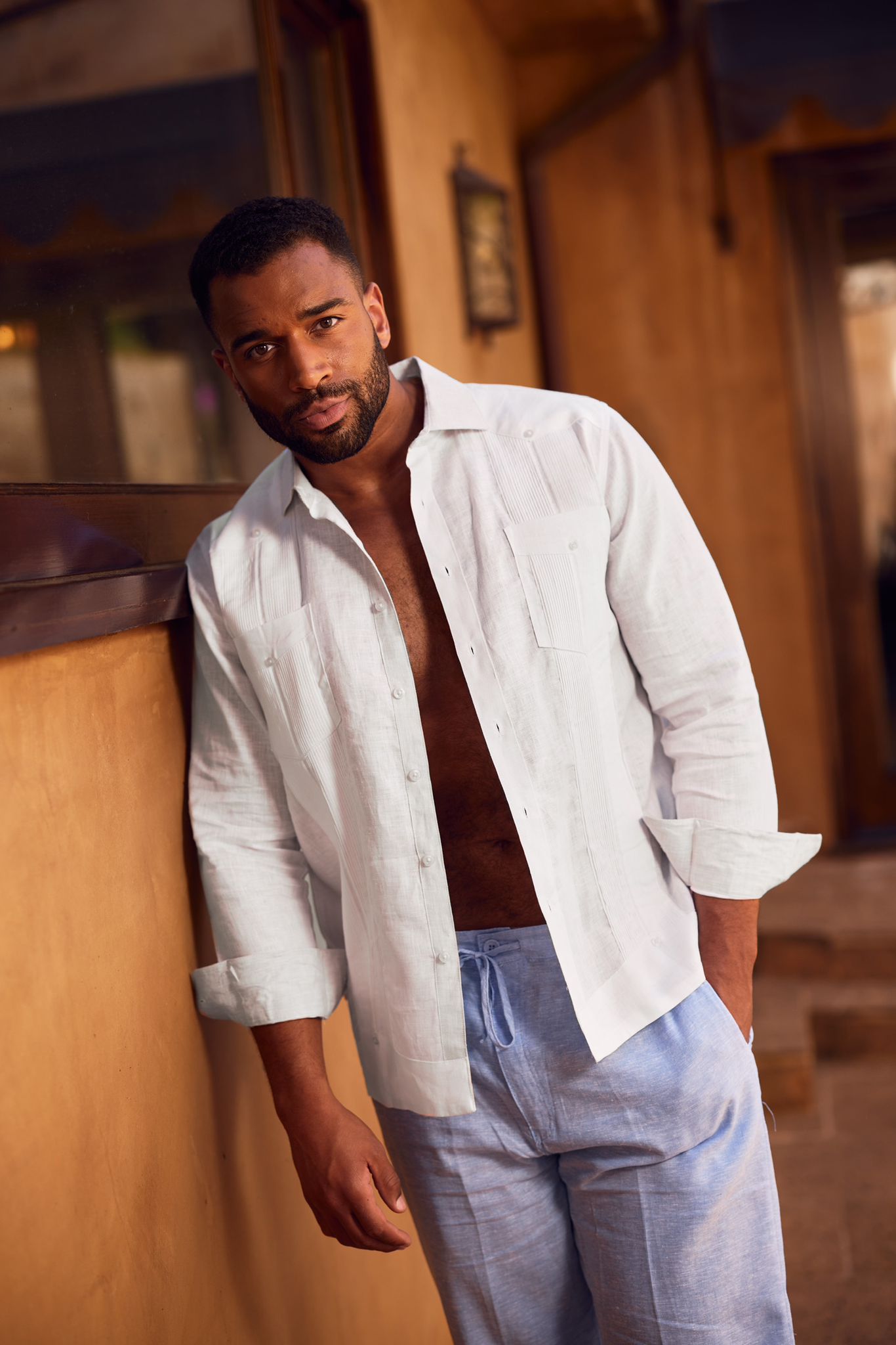 Man in an open, light blue 100% Linen Yarn Dyed Two Pocket Guayabera Shirt with long sleeves, leaning.