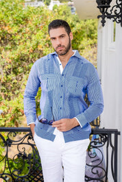 A man wears a blue striped 100% Linen Contrast Panel Guayabera Shirt with long sleeves and white linen pants.
