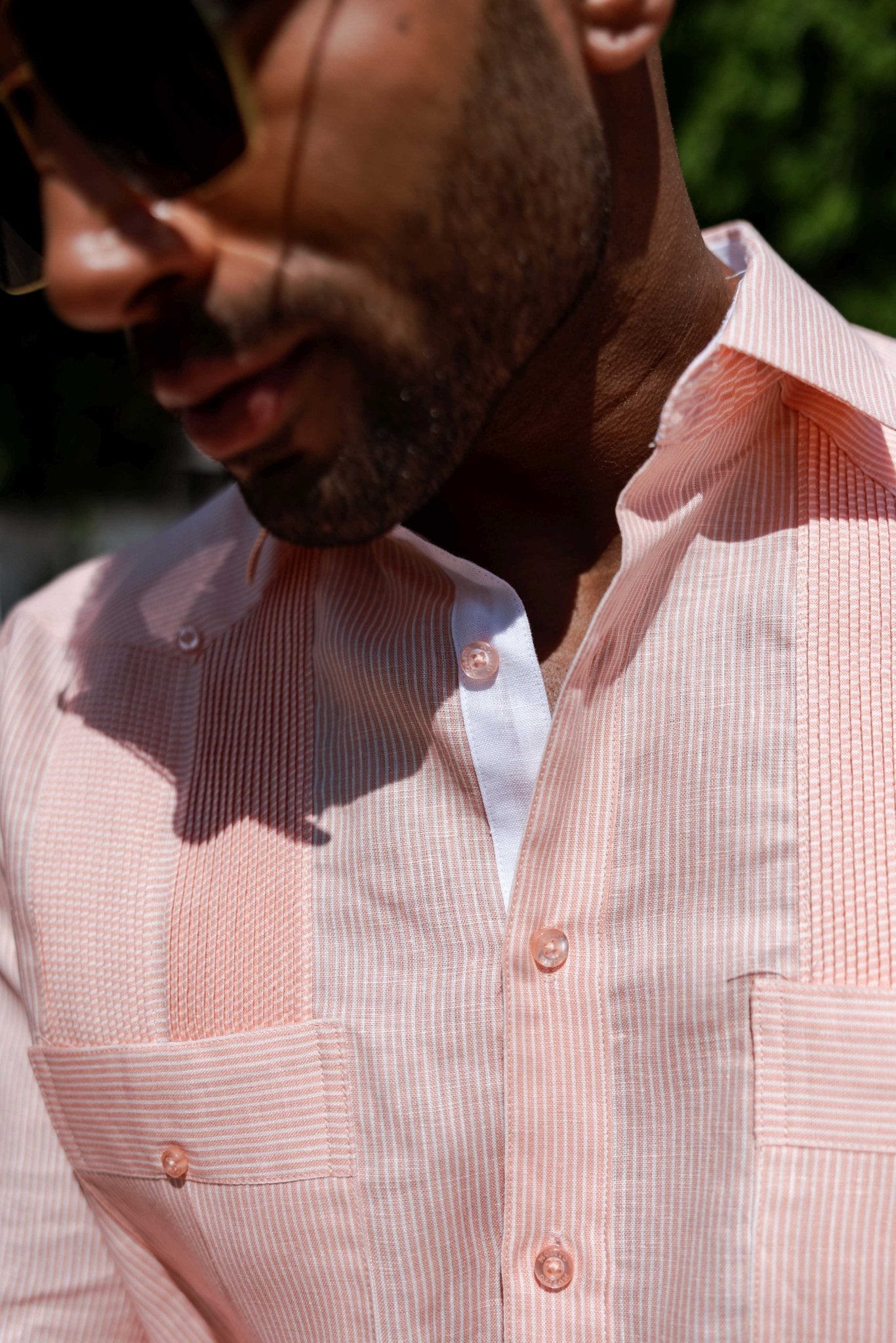 Close-up of a man wearing a striped salmon 100% Linen Contrast Panel Guayabera Shirt with a white collar.