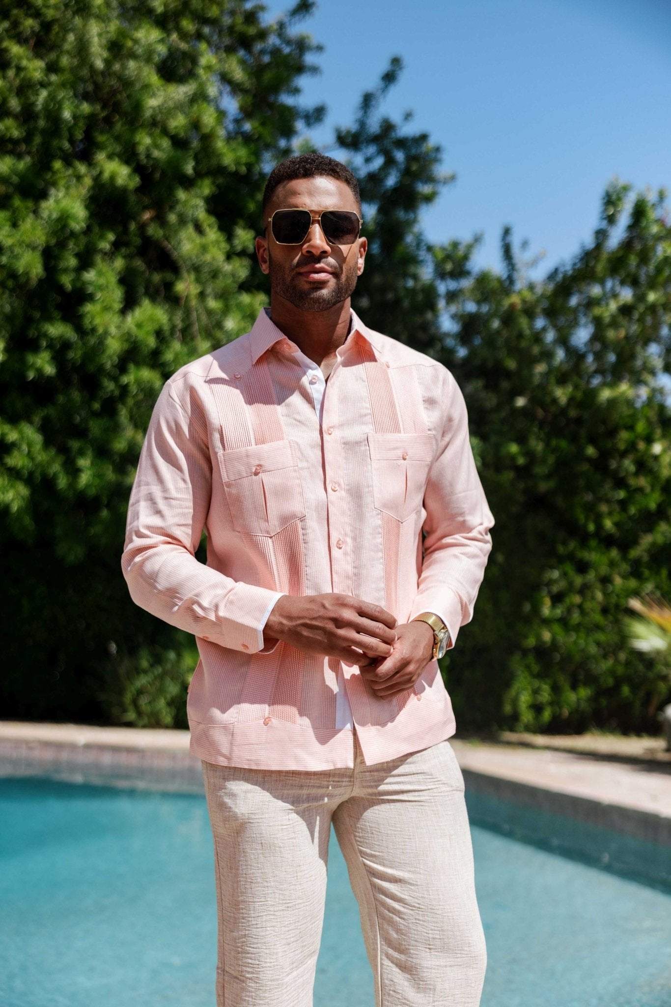Front view of a man wearing the 100% Linen Contrast Panel Guayabera Shirt Long Sleeve in light pink with sunglasses.