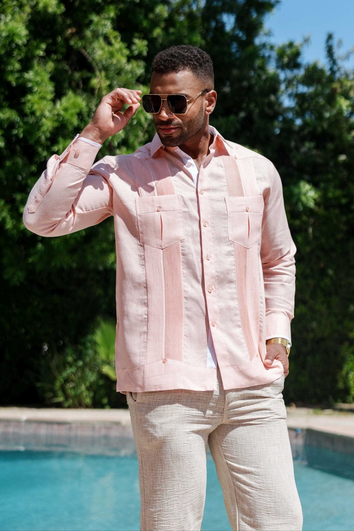 Man in a light pink 100% Linen Contrast Panel Guayabera Shirt with long sleeves, sunglasses, and tan pants.