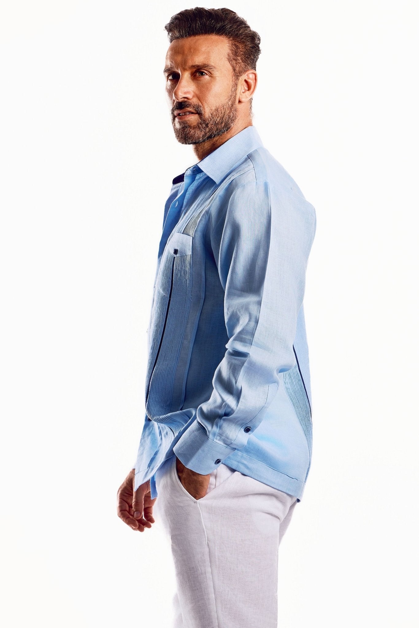 Profile view of a man wearing a blue, linen, long sleeve, contrast trim Guayabera shirt.