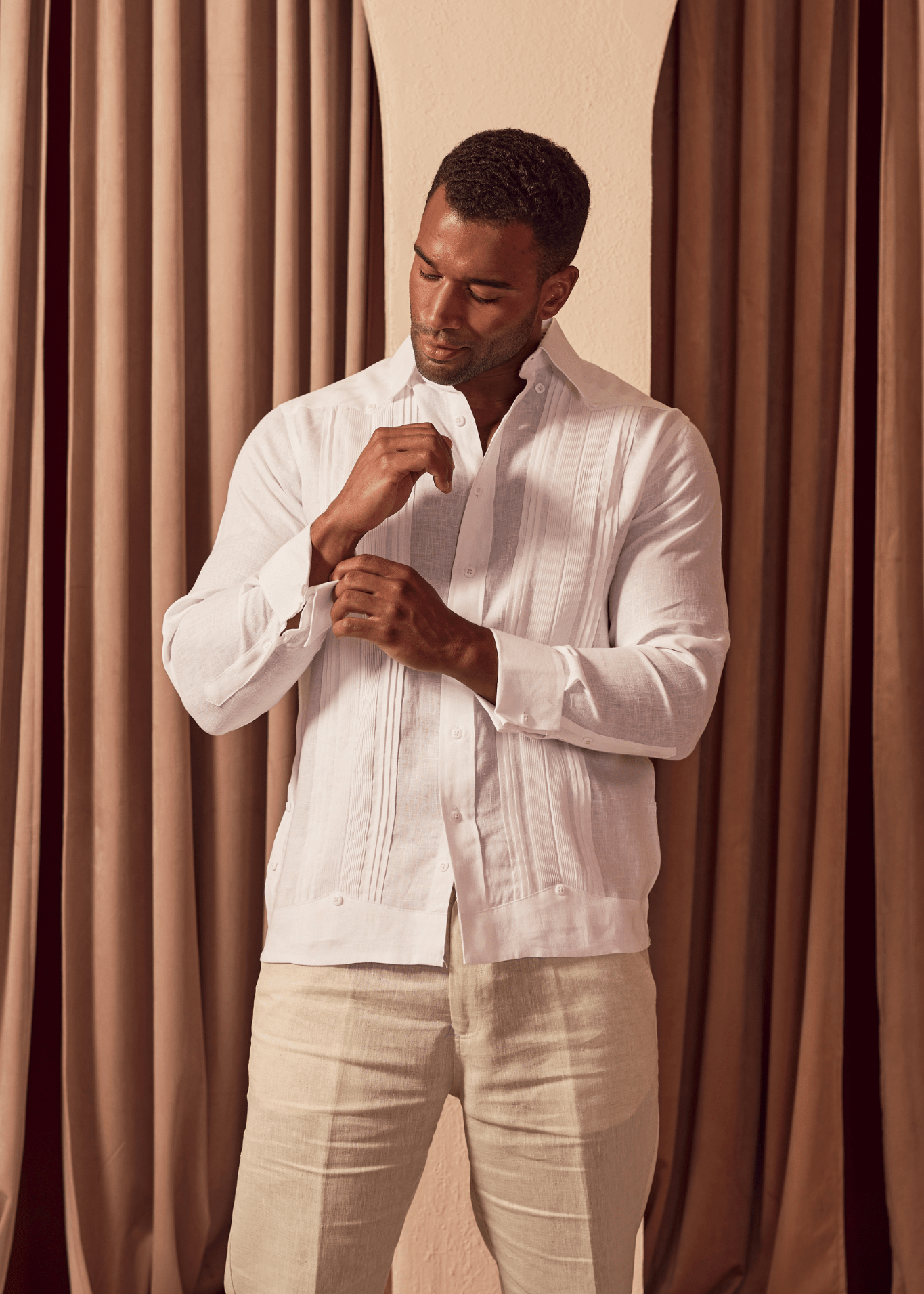 Model in white Men's Linen Formal Guayabera Long Sleeve Pleated Shirt, adjusting French cuff.