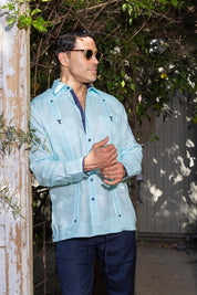 A man wearing a light blue Men's Long Sleeve Linen Guayabera Shirt with sunglasses, showing the breathable fabric and heritage style for warm evenings.
