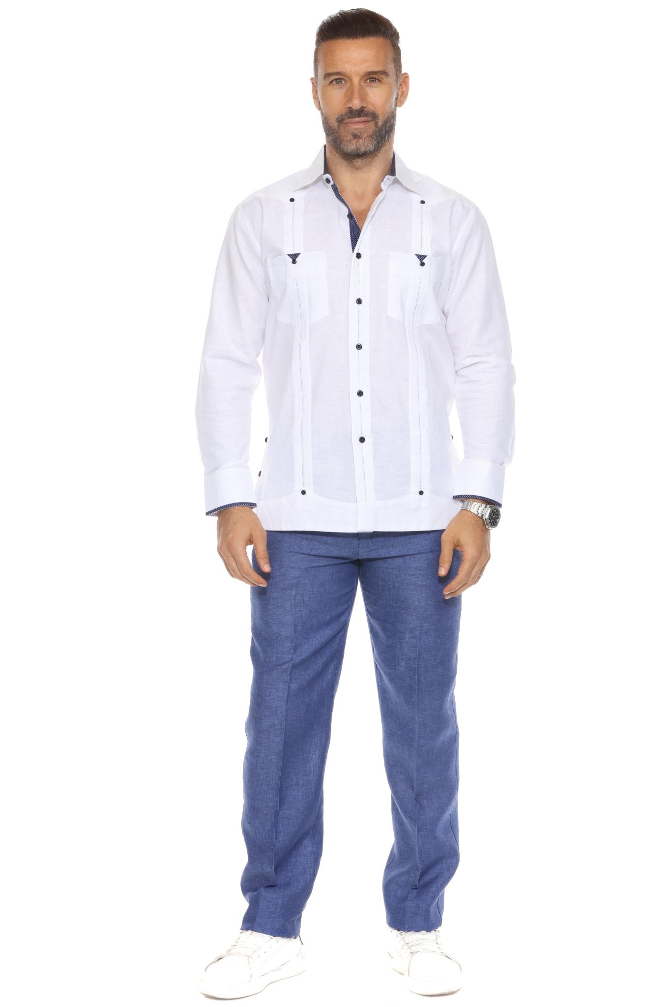 A man wearing a white Men’s Long Sleeve Linen Guayabera Shirt with blue linen trousers and white sneakers for a modern resort look.