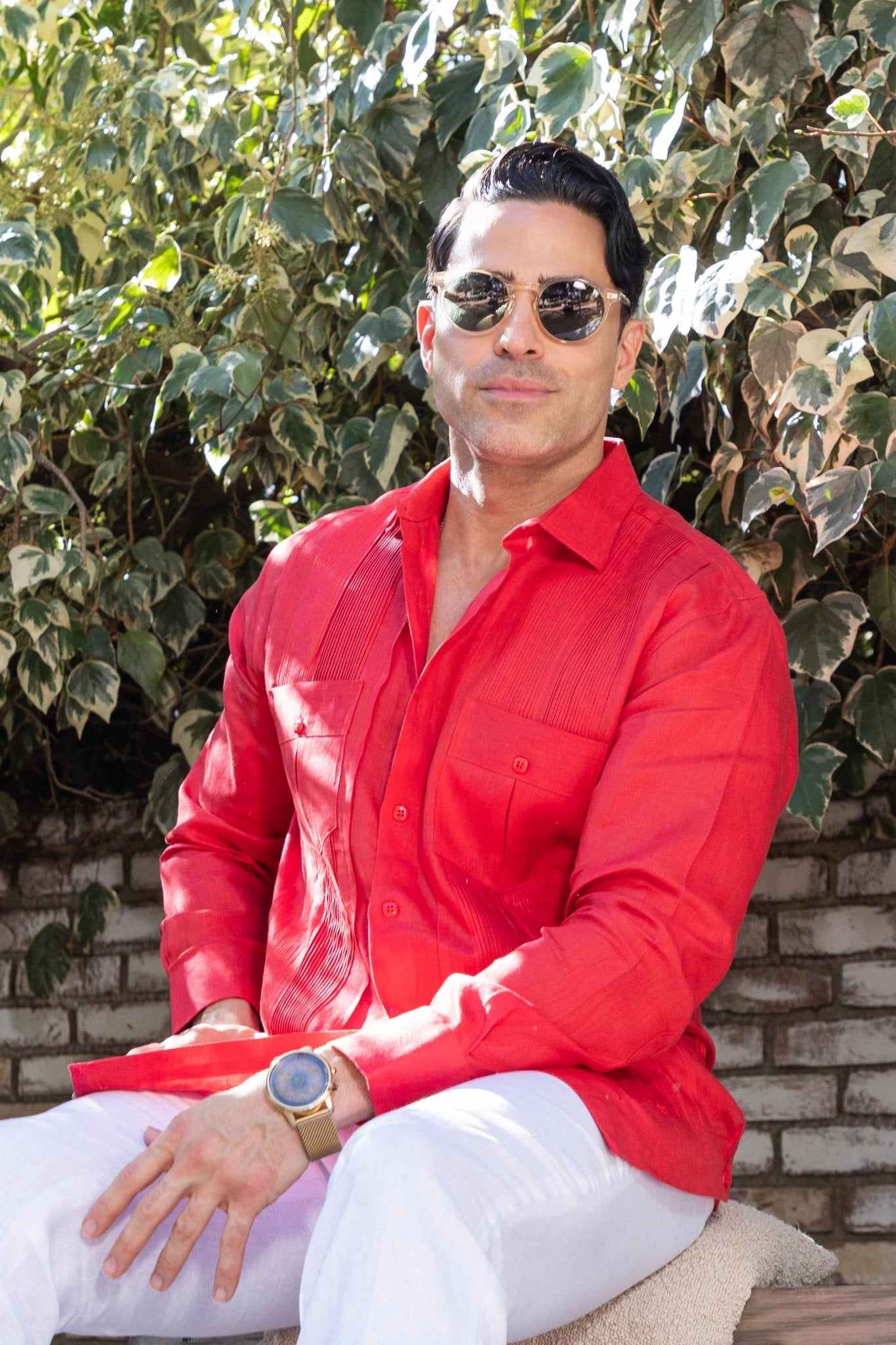 Man wears a red Yarn Dyed Linen Guayabera shirt with multi-pleats and two pockets, and white pants.