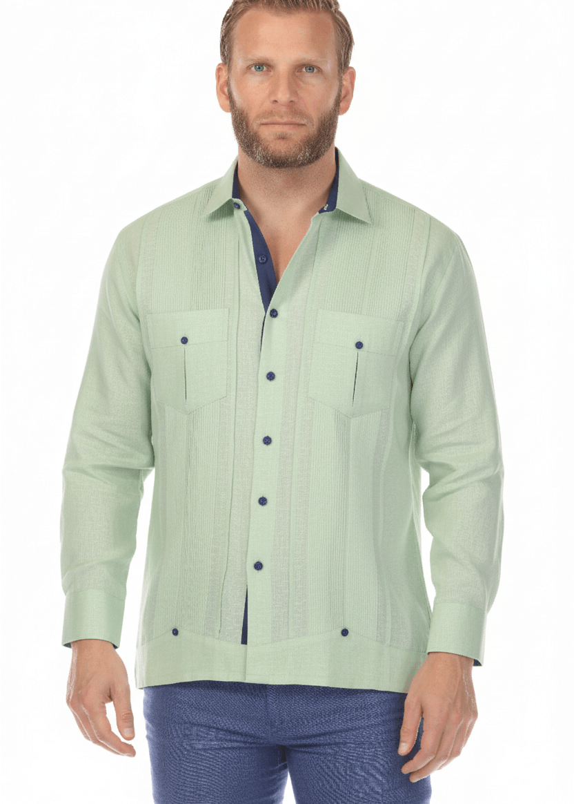 Men's sage green linen guayabera shirt with navy contrast trim and two chest pockets, front-facing studio shot paired with navy blue trousers on white background