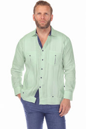 Front view of a man wearing the sage green 100% Linen Contrast Panel Guayabera Shirt Long Sleeve with navy trim, hand in pocket.