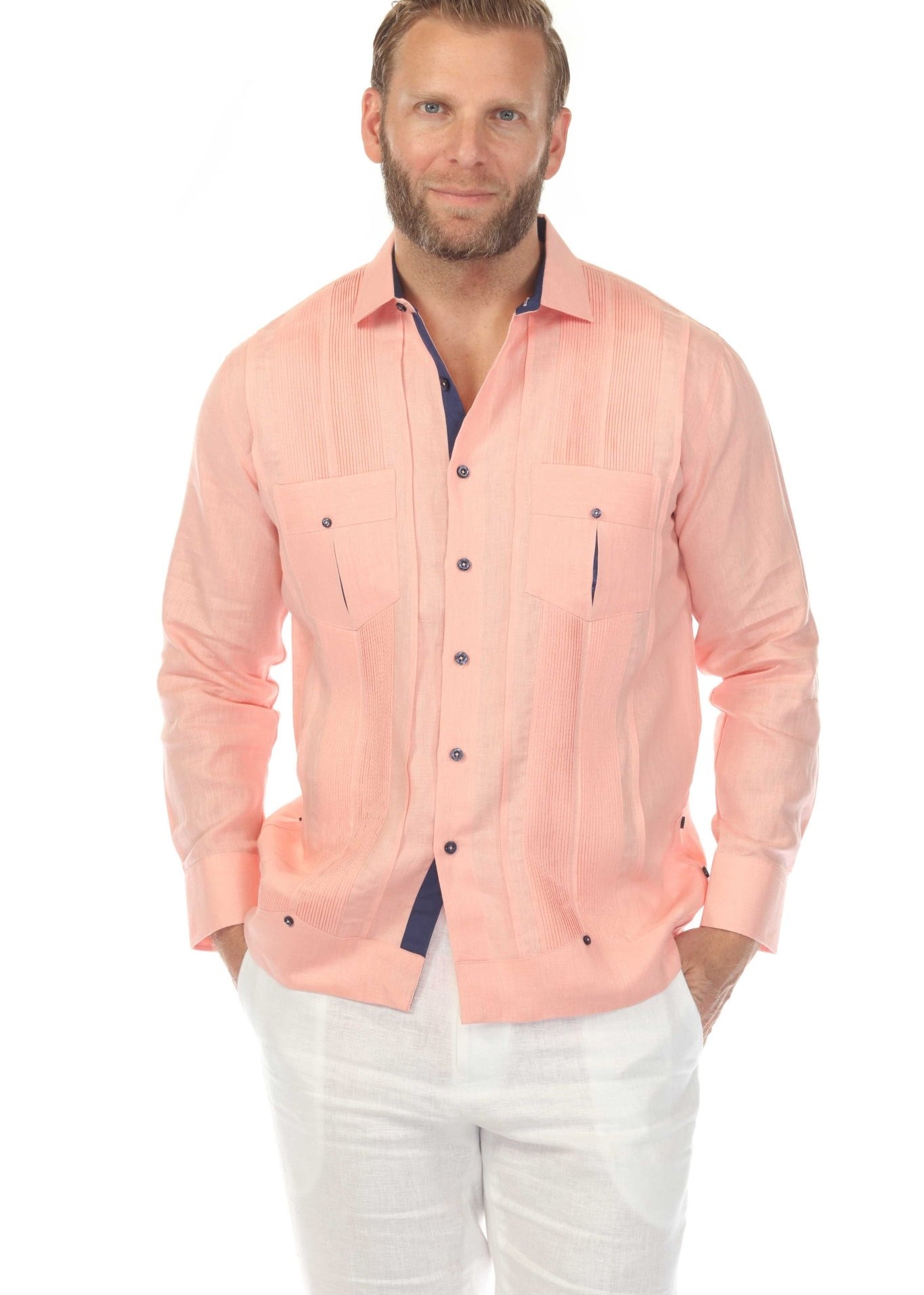 Men's premium linen guayabera shirt in salmon pink with pleated front panels and navy detail, side angle studio view showing tailored drape on white background