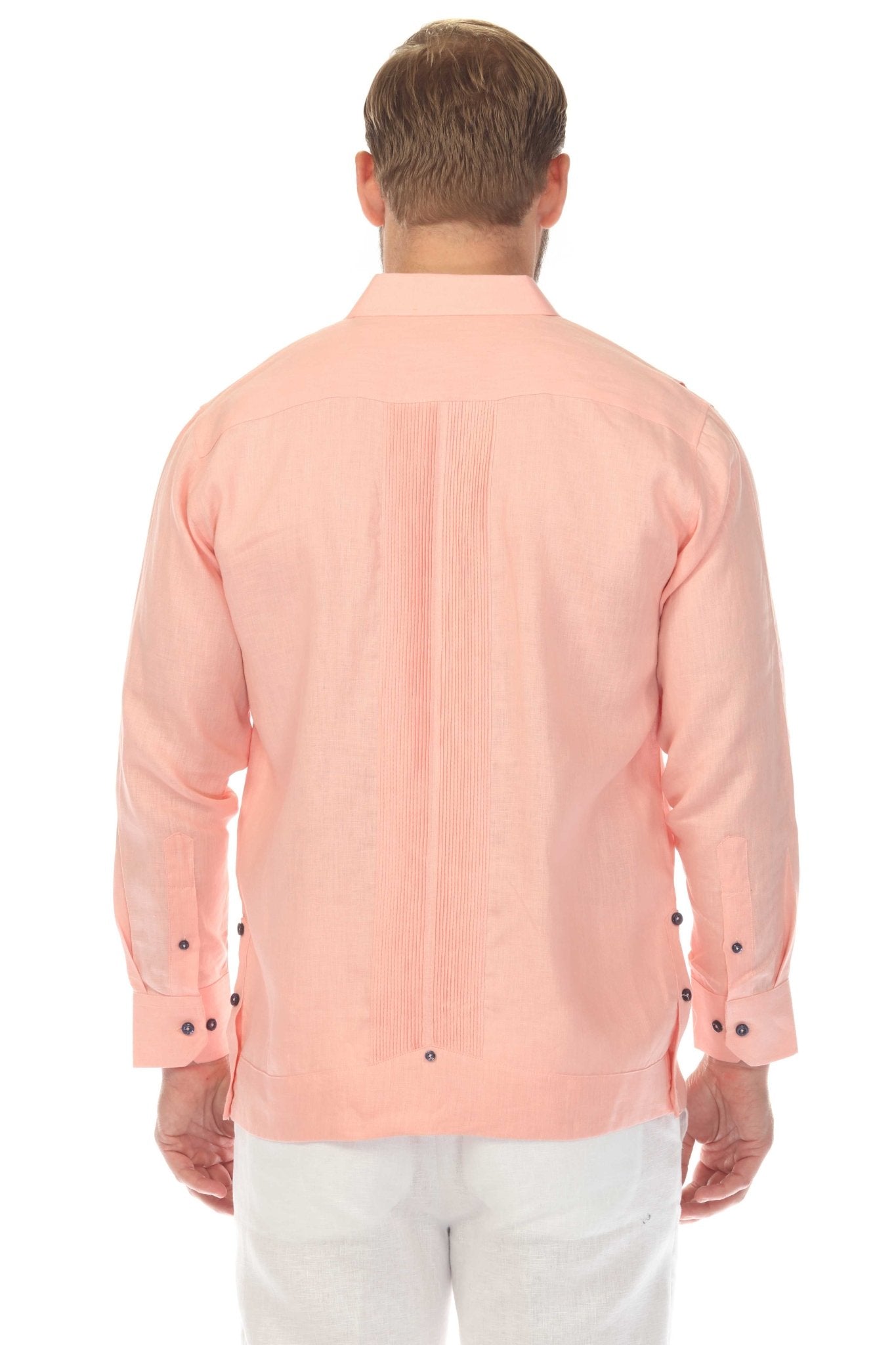 Back view of men's salmon pink linen guayabera shirt showing center pleat detail and navy cuff buttons, model standing in clean white studio setting