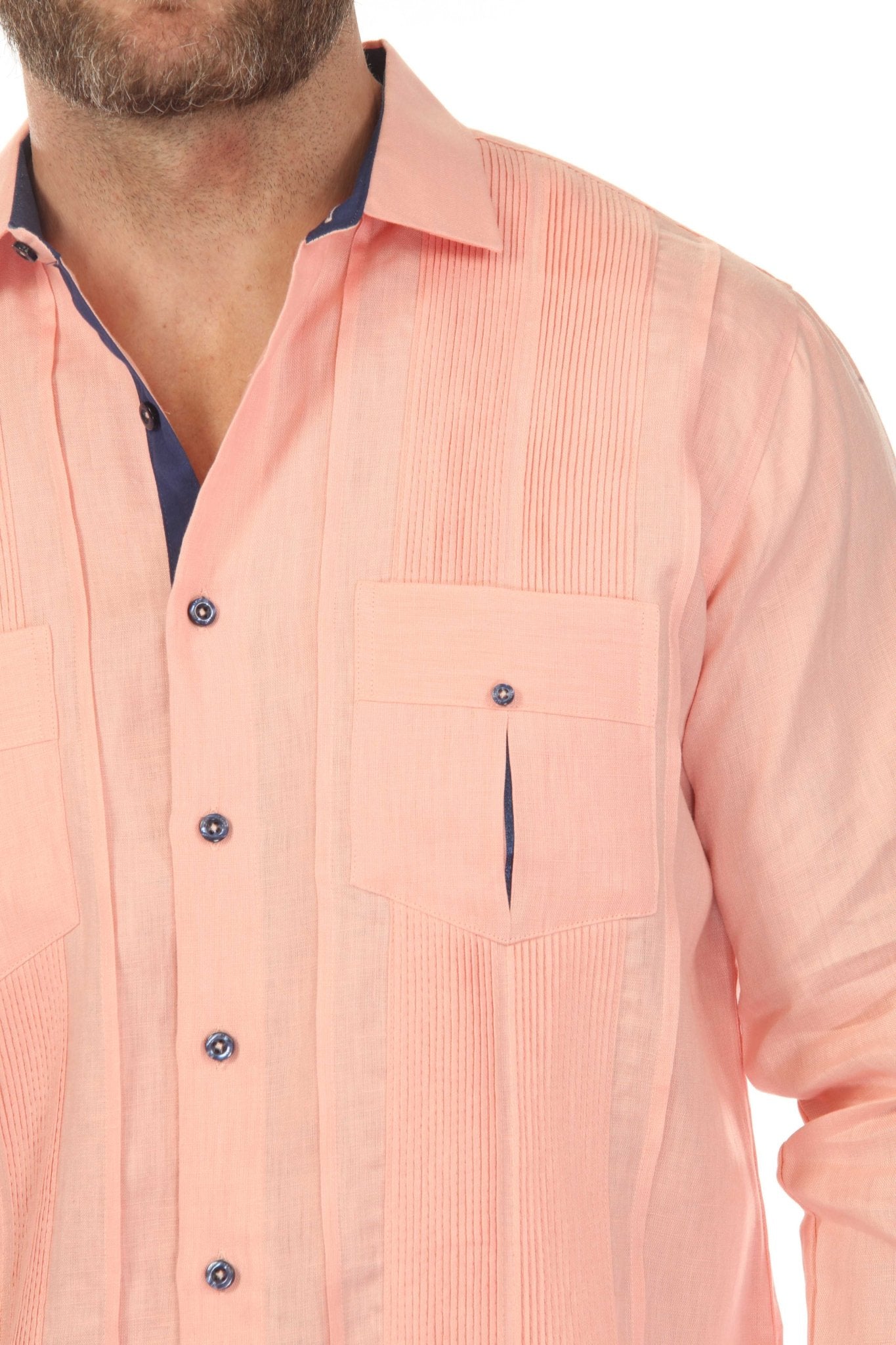 Close-up chest detail of men's salmon linen guayabera shirt showing hand-finished two chest pockets with navy contrast trim and pleated front bib on white background