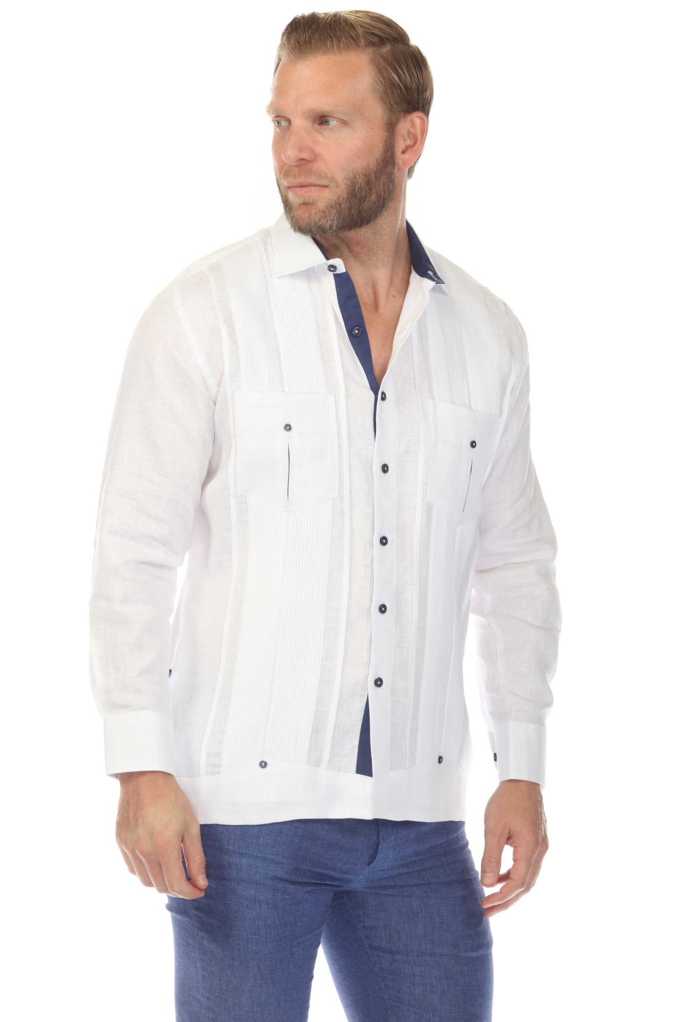 Men's white premium linen guayabera shirt with navy buttons and pleated front, three-quarter angle studio view showcasing tailored fit paired with blue denim trousers