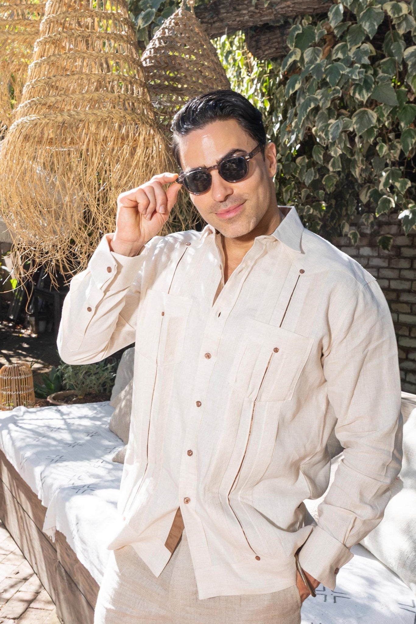 A man in a light-colored 100% Linen Contrast Panel Guayabera Shirt, long sleeve adjusts his sunglasses.