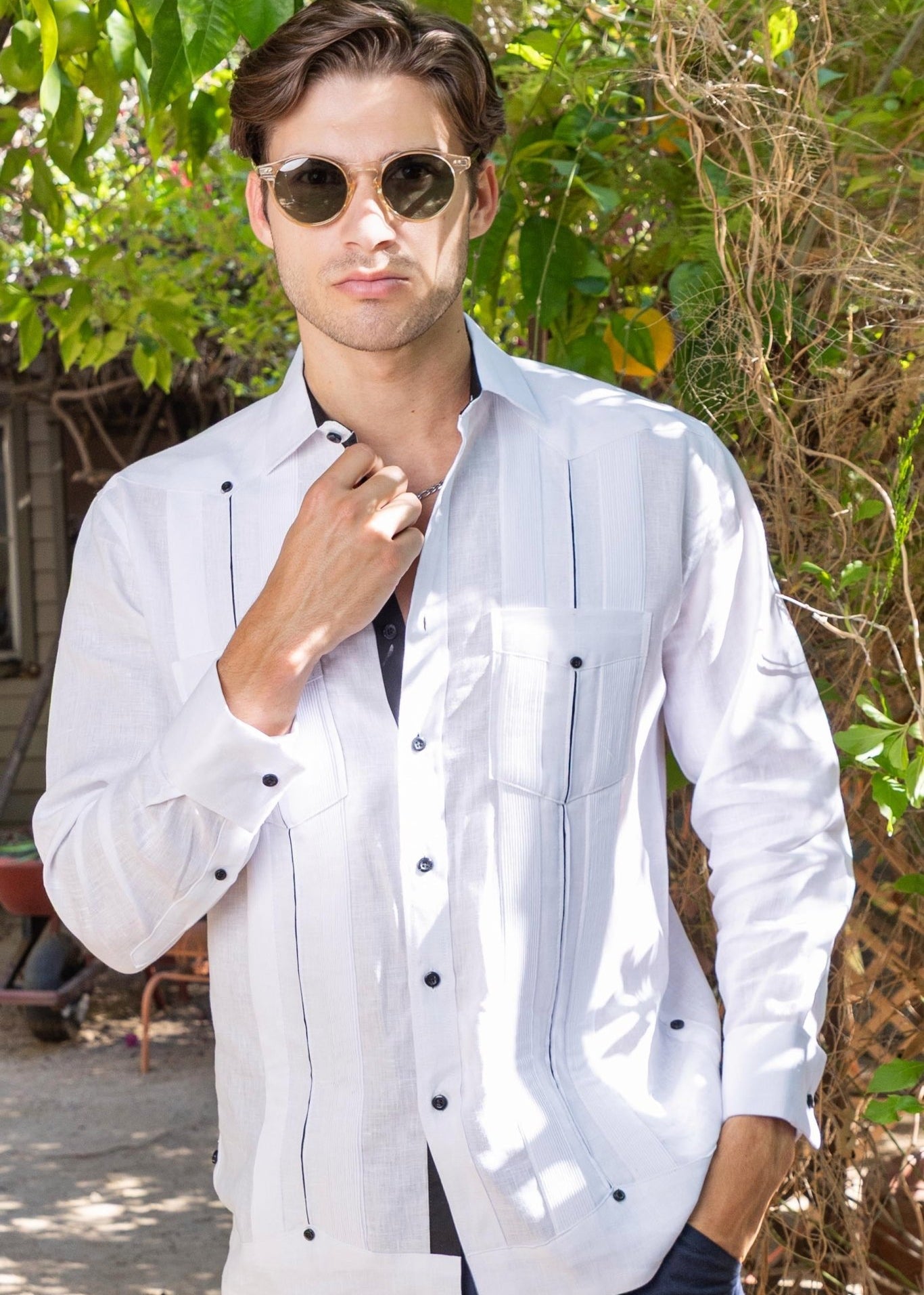 A man wears a white Men's 100% Linen Guayabera with black contrast taping and stylish French cuffs.