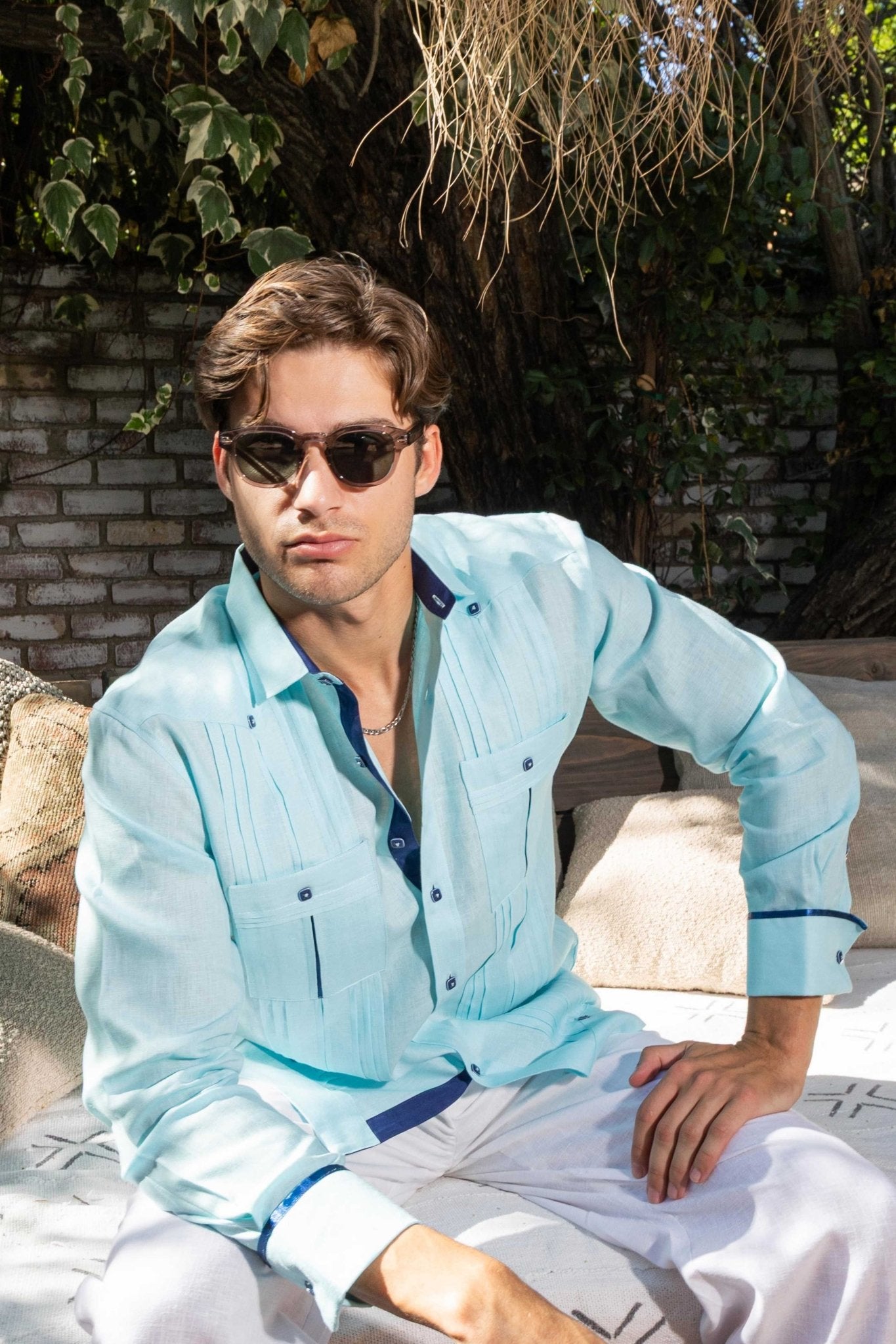 A man wears a light blue 100% Linen Contrast Panel Guayabera Shirt Long Sleeve with dark blue trim, shown at a medium view.