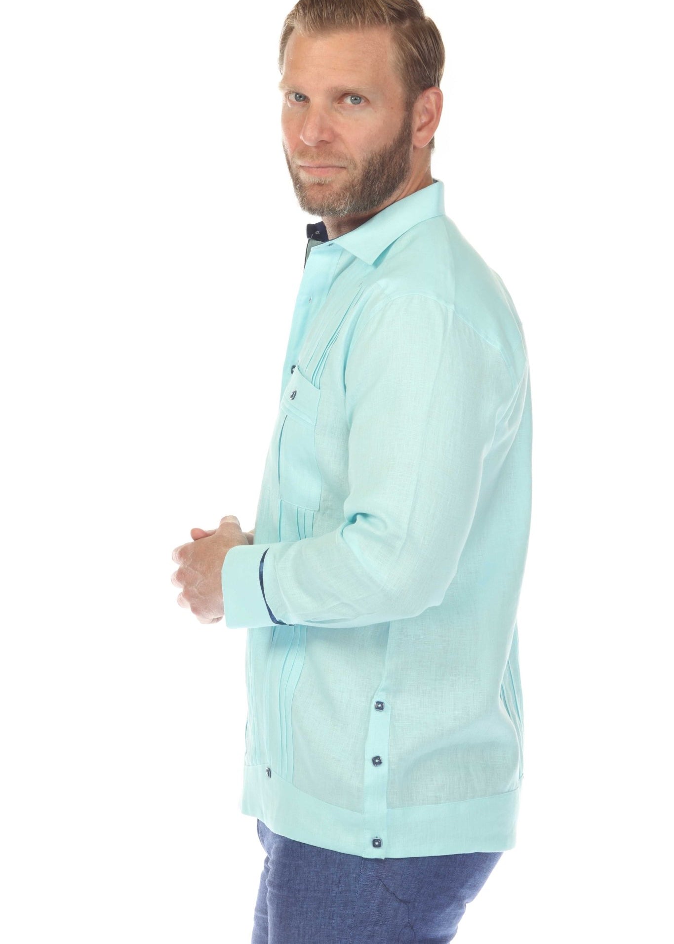 A man models the light blue linen guayabera shirt, side view showing pleating, pockets, and contrast trim.