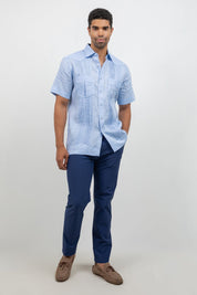 Man wearing a light blue short-sleeve shirt and dark blue pants on a white background