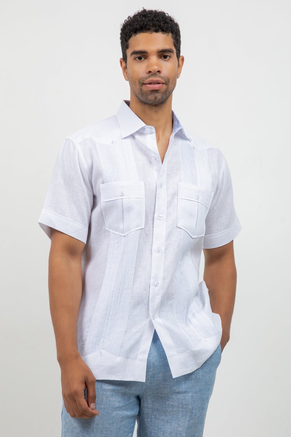 Man wearing a white short-sleeve shirt and light blue jeans against a plain background