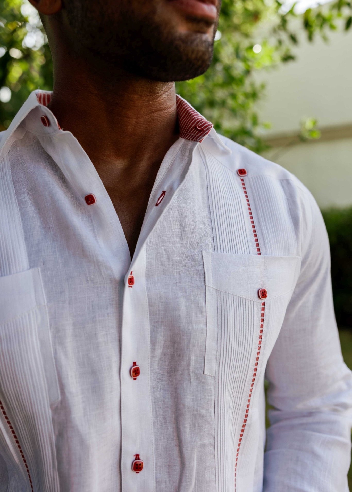 Close-up of the collar and red button detailing on a Men’s Mojito white linen guayabera shirt.
