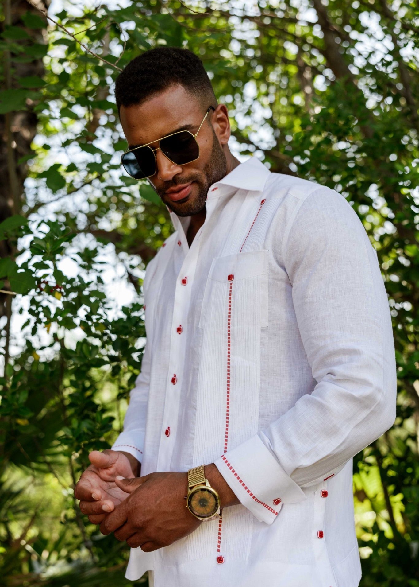 Men's 100% white linen guayabera shirt with red contrast trim and French cuffs, lifestyle view in a tropical setting.