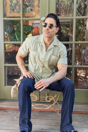 Man seated in a light green, two-pocket, pleated Men's Two-Pocket Cross-Dye Guayamisa Shirt.