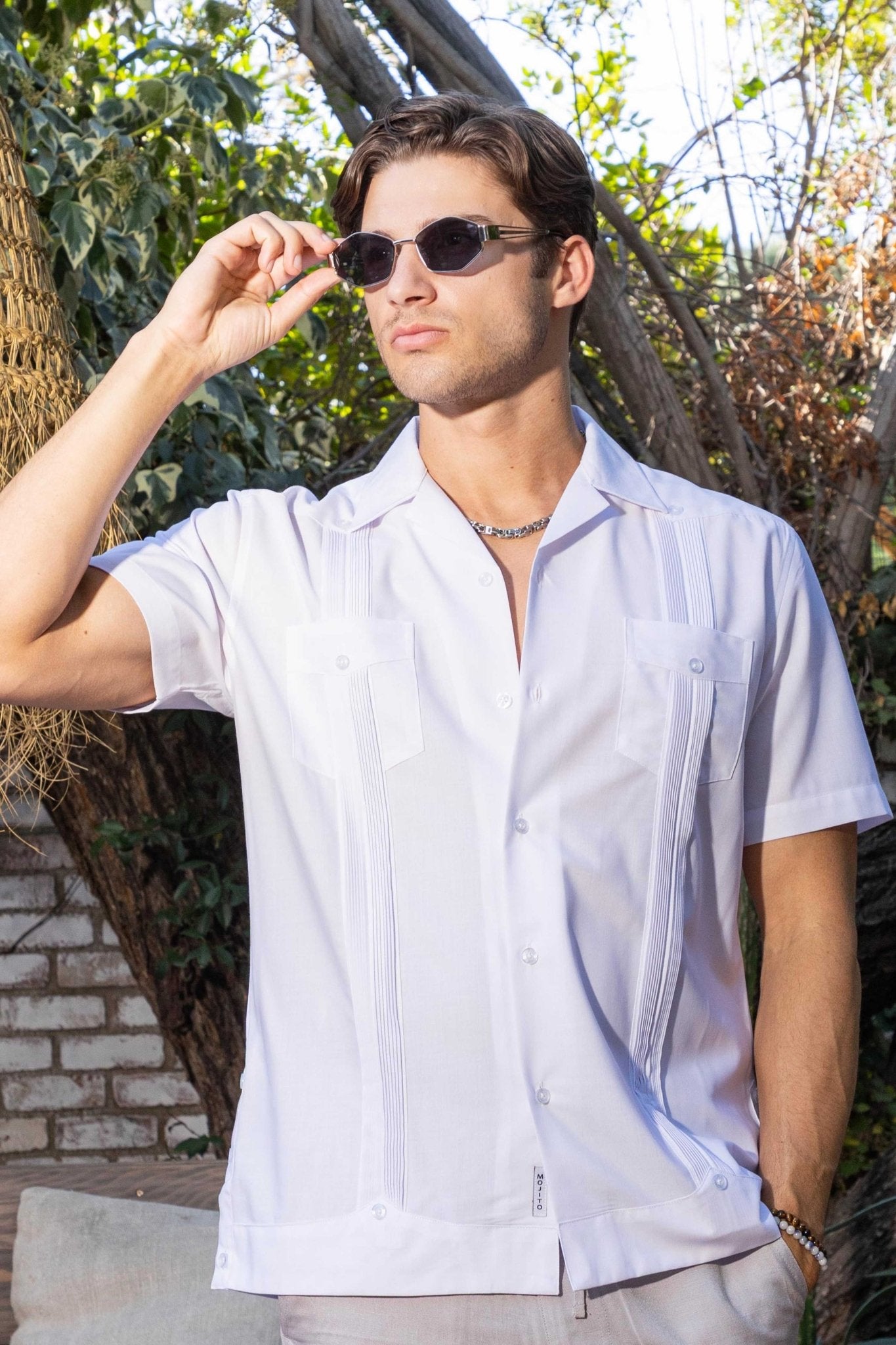 A man wears a white Men’s Two-Pocket Cross-Dye Guayamisa Shirt with Pleats and sunglasses outside.