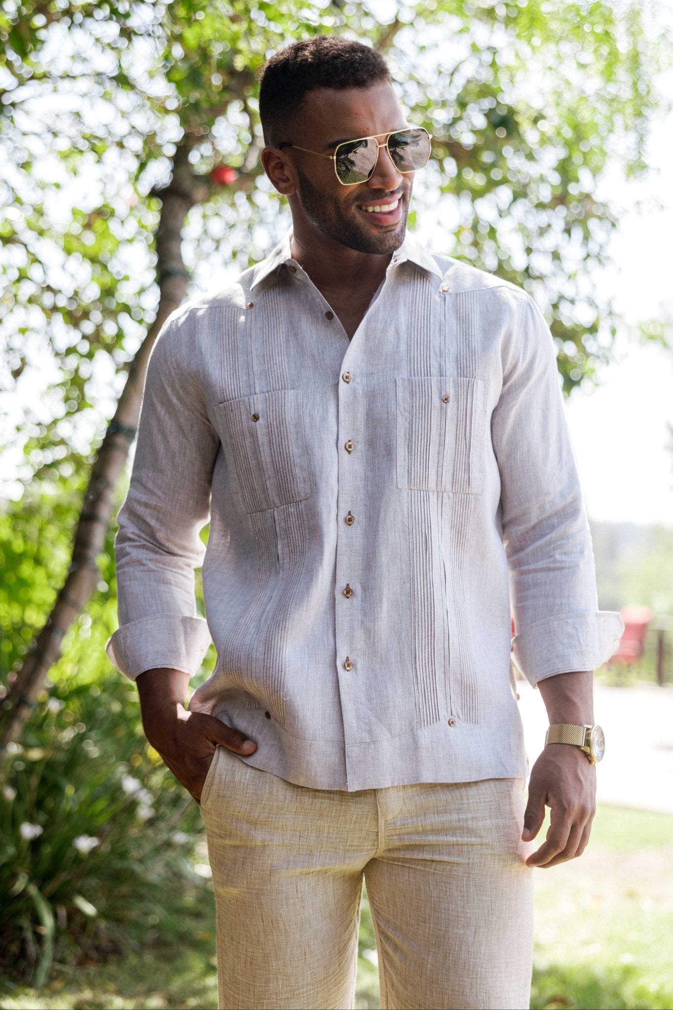 A smiling man wears a light tan Men’s 100% Linen Guayabera Shirt with long sleeves and heritage pleats.