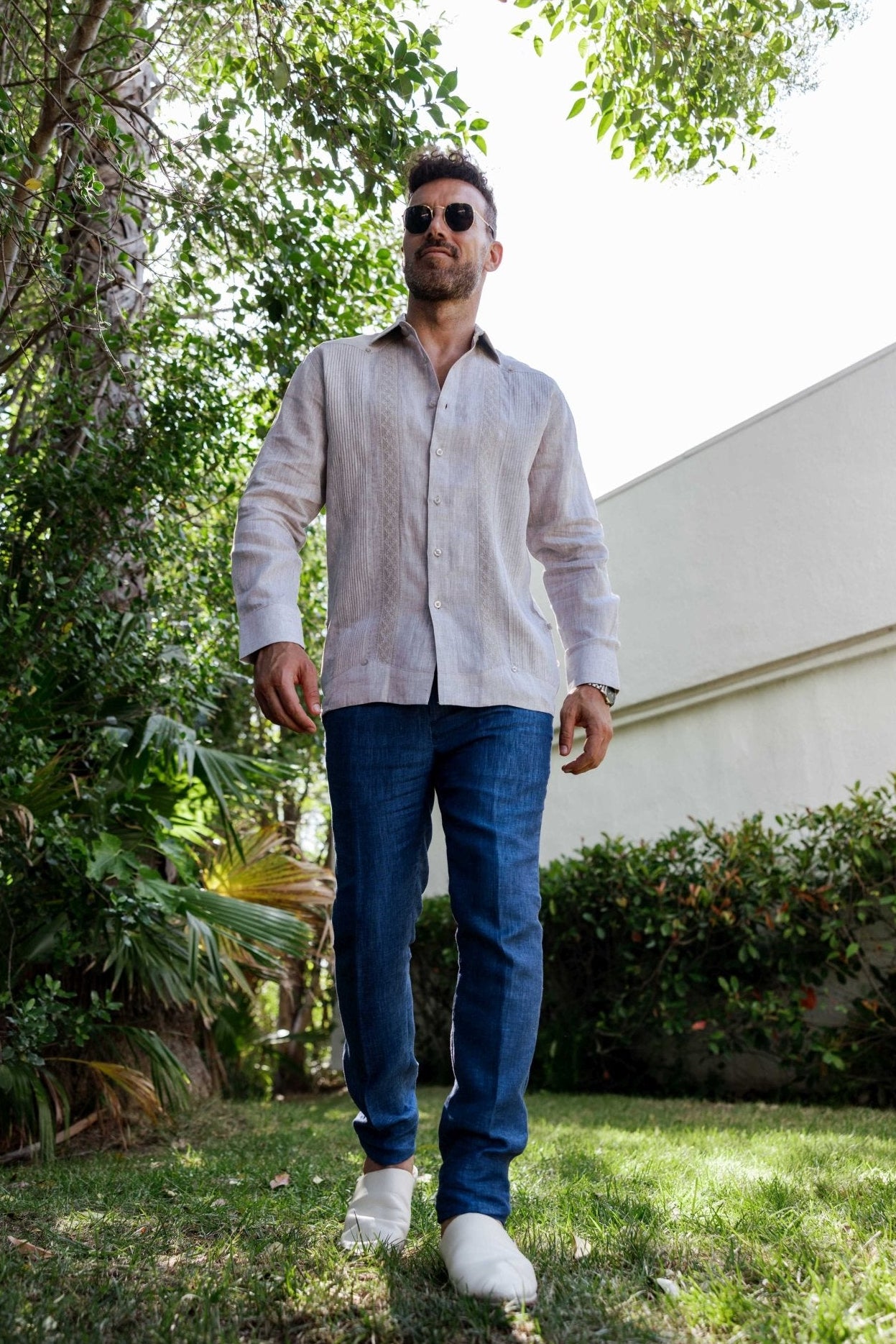 Low angle of a man wearing the 100% Linen Contrast Panel Guayabera Shirt long sleeve in natural with jeans.