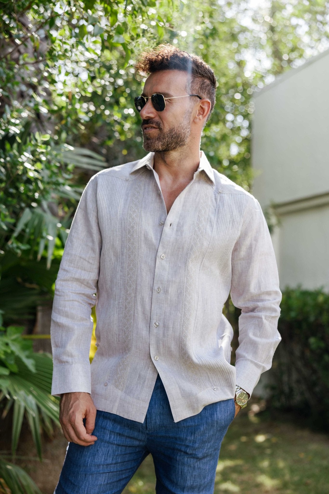 A man in a light tan, long-sleeve 100% Linen Contrast Panel Guayabera Shirt with blue pants.
