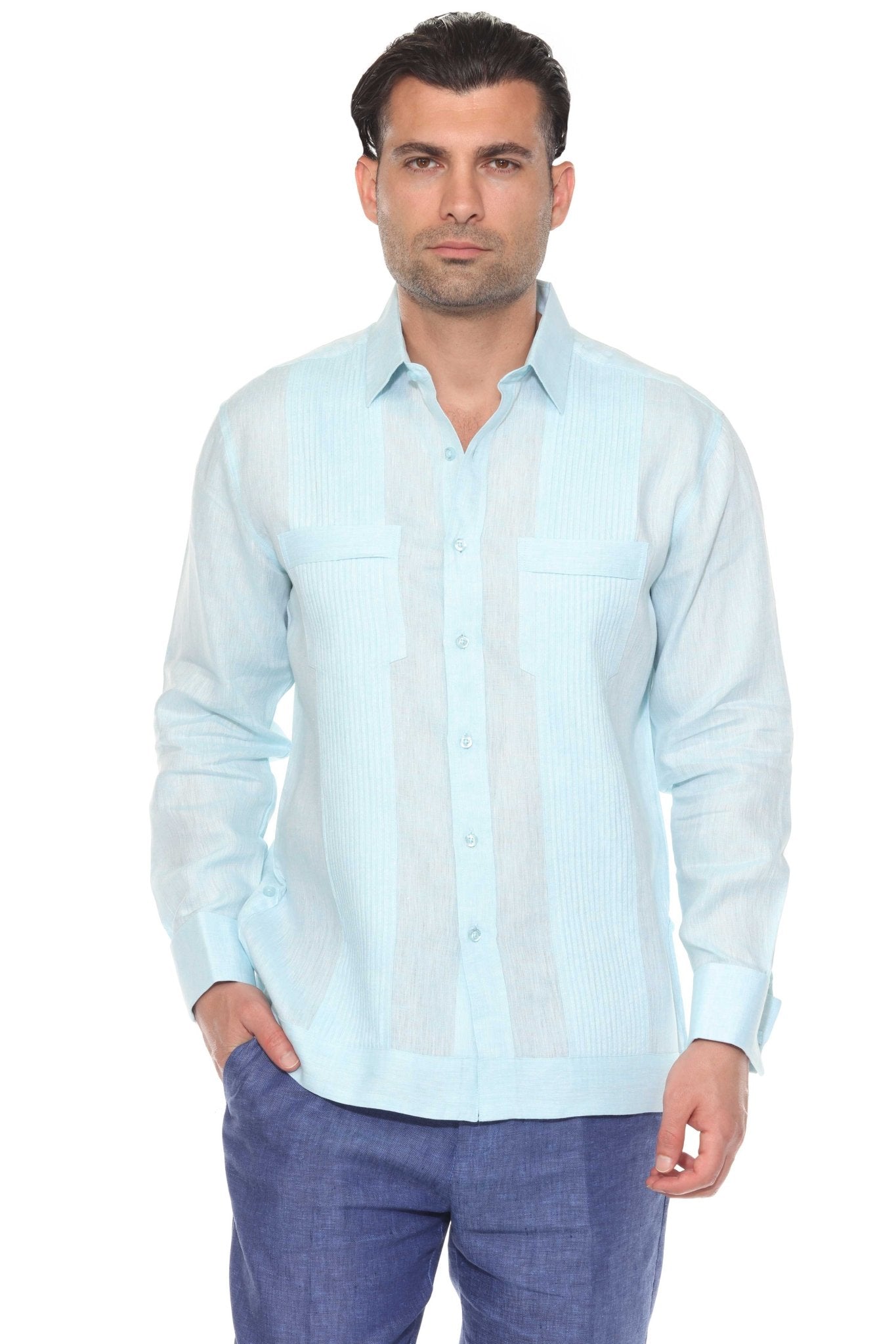 Studio photo of a man wearing a light blue long sleeve guayabera with tonal pleats and blue linen trousers.