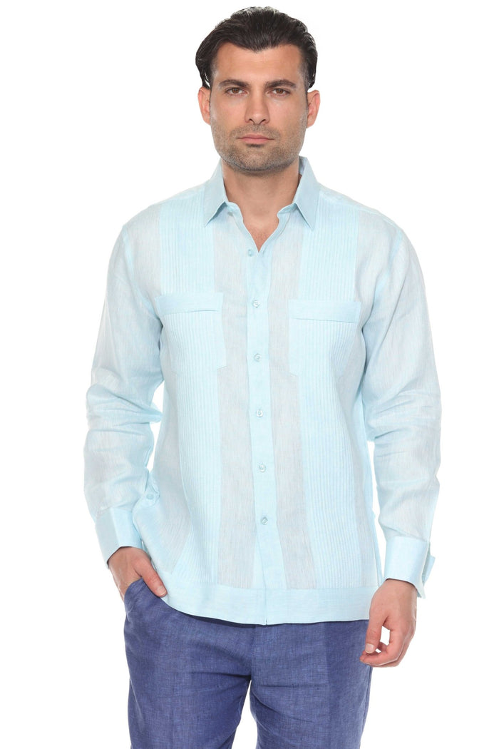 A man wearing a beige long sleeve linen guayabera with white trousers standing outdoors.