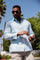 A man wearing a light blue long sleeve 100% linen guayabera with vertical tonal pleats standing outdoors.