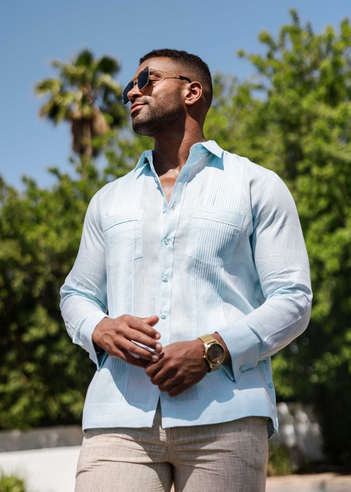 A man standing outside wearing a light blue long sleeve guayabera made of 100% linen with front pleat details.