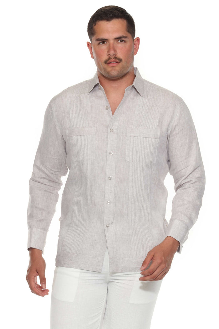 A man wearing a beige long sleeve linen guayabera with white trousers standing outdoors.