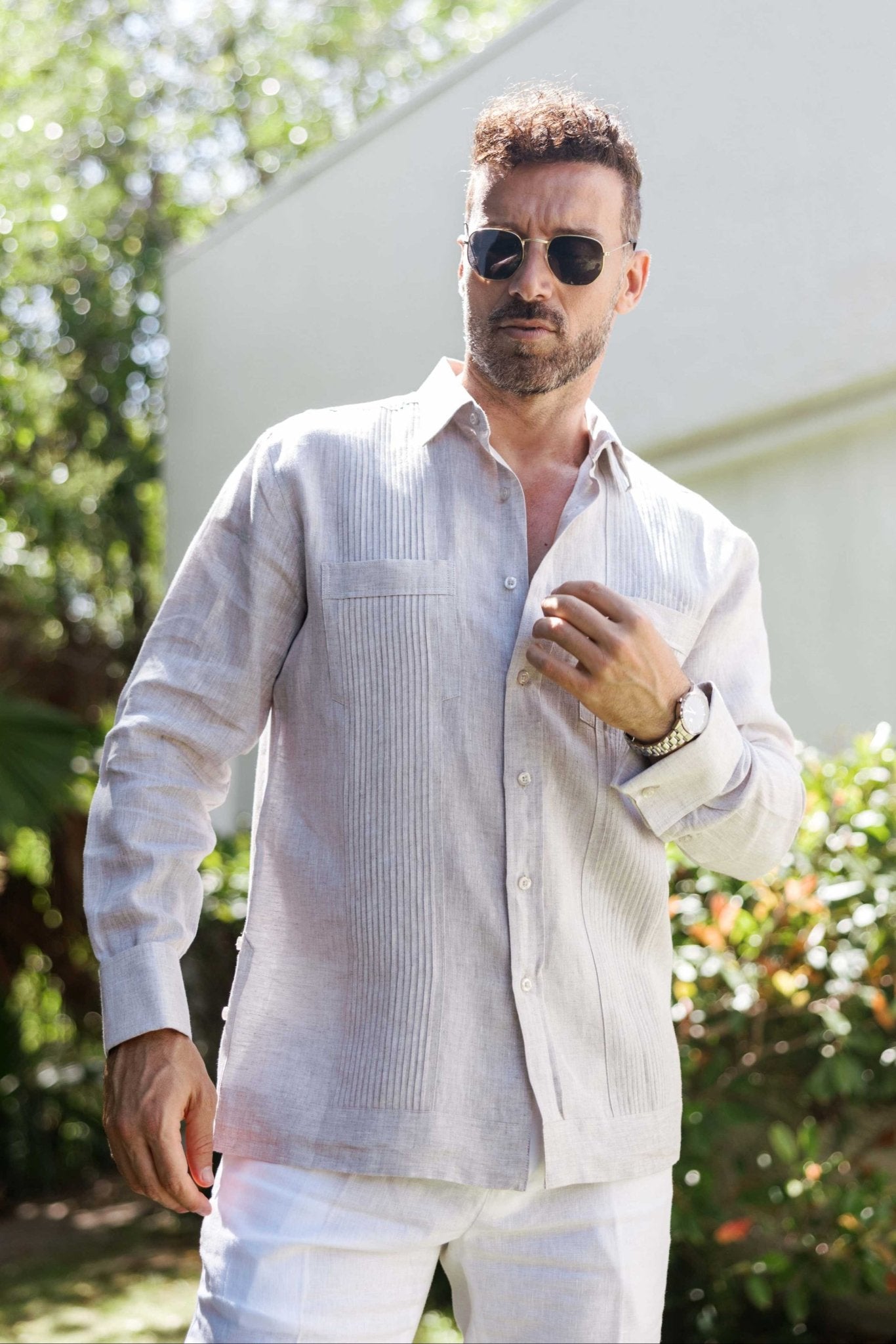 A man adjusting his tan 100% linen long sleeve guayabera featuring modern tonal pleats.