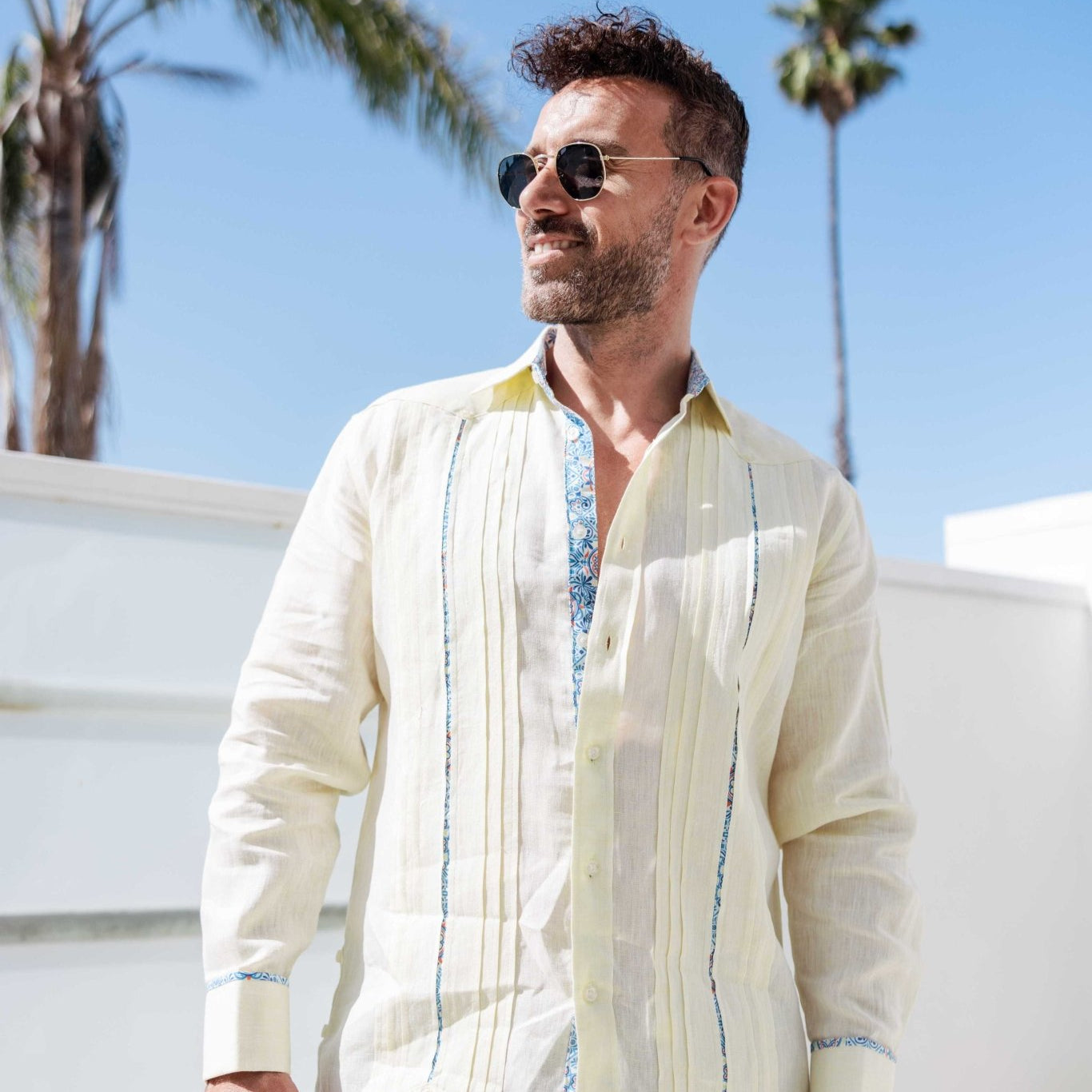 Man wearing a cream 100% linen long sleeve guayabera shirt with blue embroidery and signature pleated front.