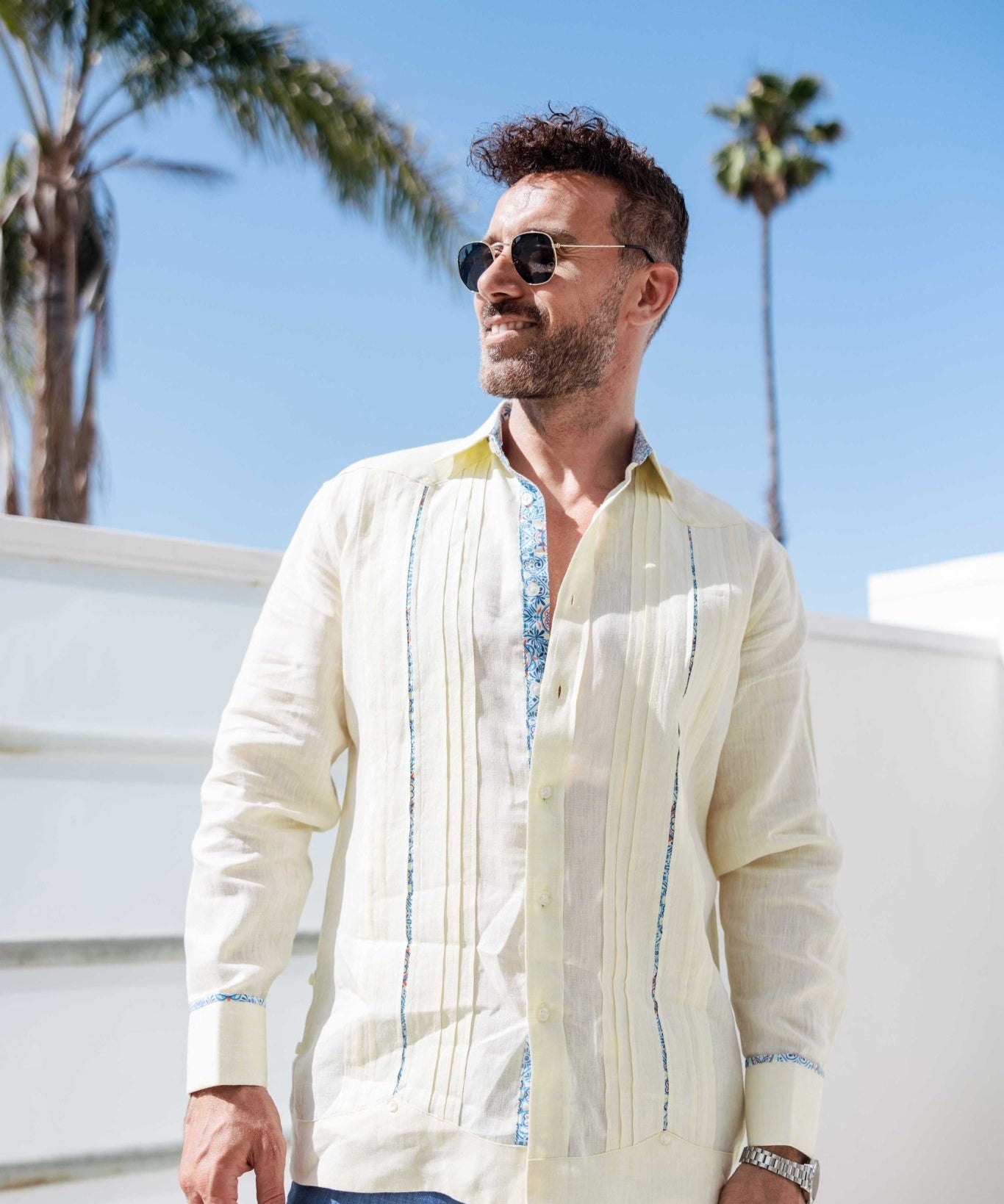 Man wearing a cream 100% linen long sleeve guayabera shirt with blue embroidery and signature pleated front.