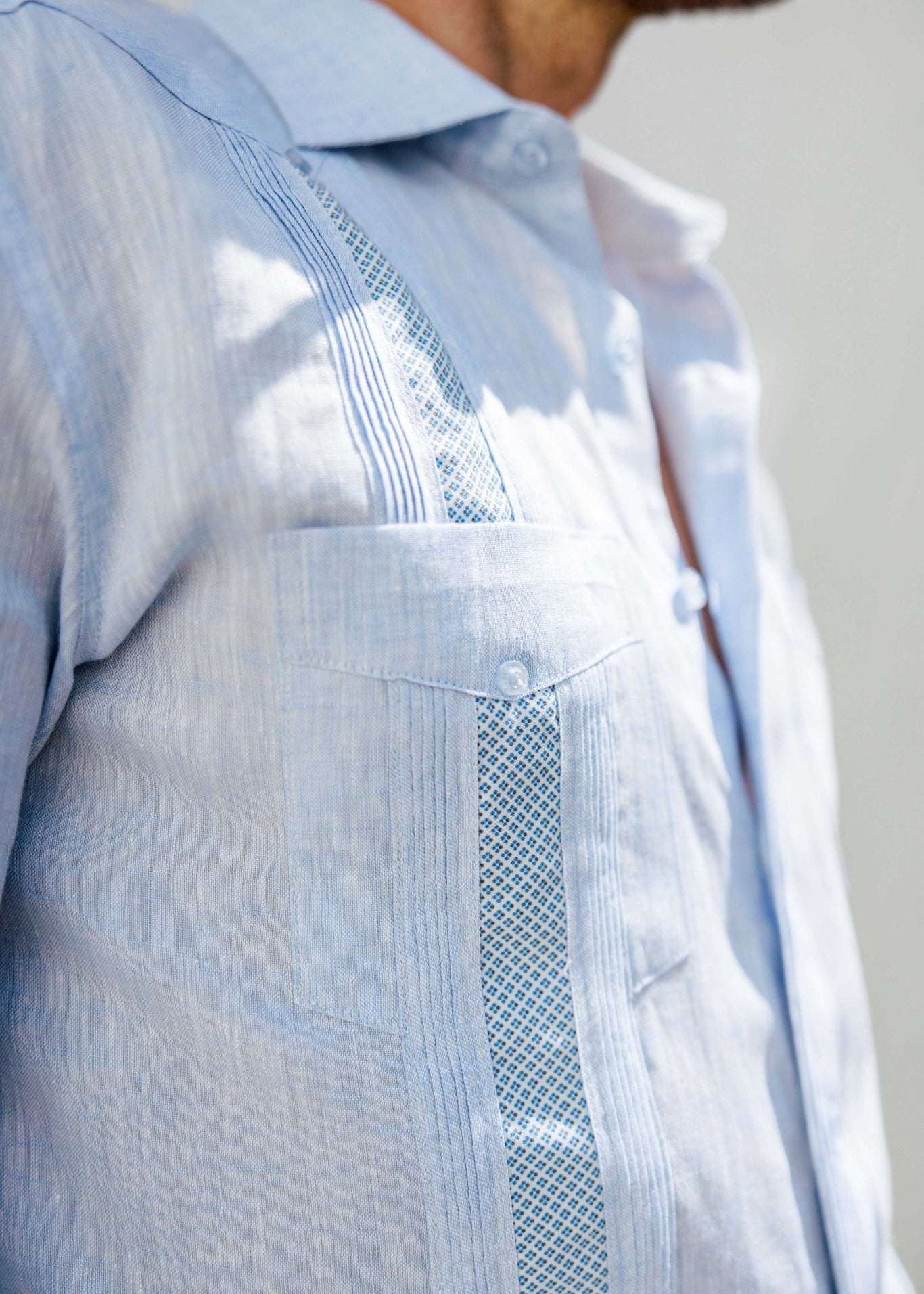 Close-up of a light blue linen Men's Guayabera Shirt showing artisan embroidery detail and pocket.
