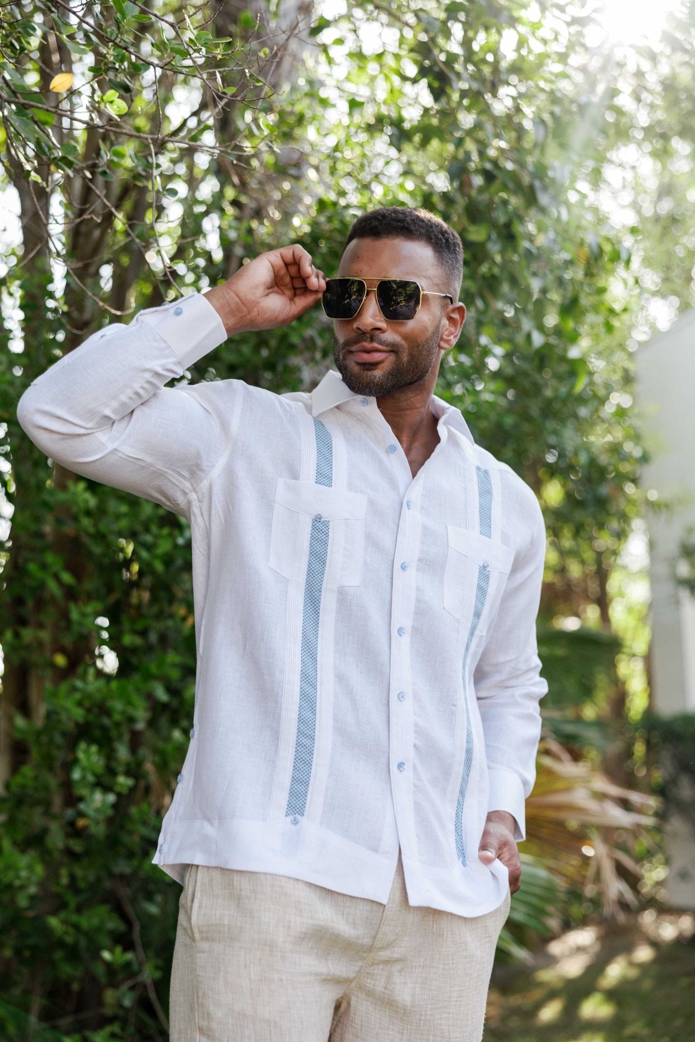Man in a white linen long sleeve Guayabera shirt with light blue embroidery, outdoors, wearing sunglasses.