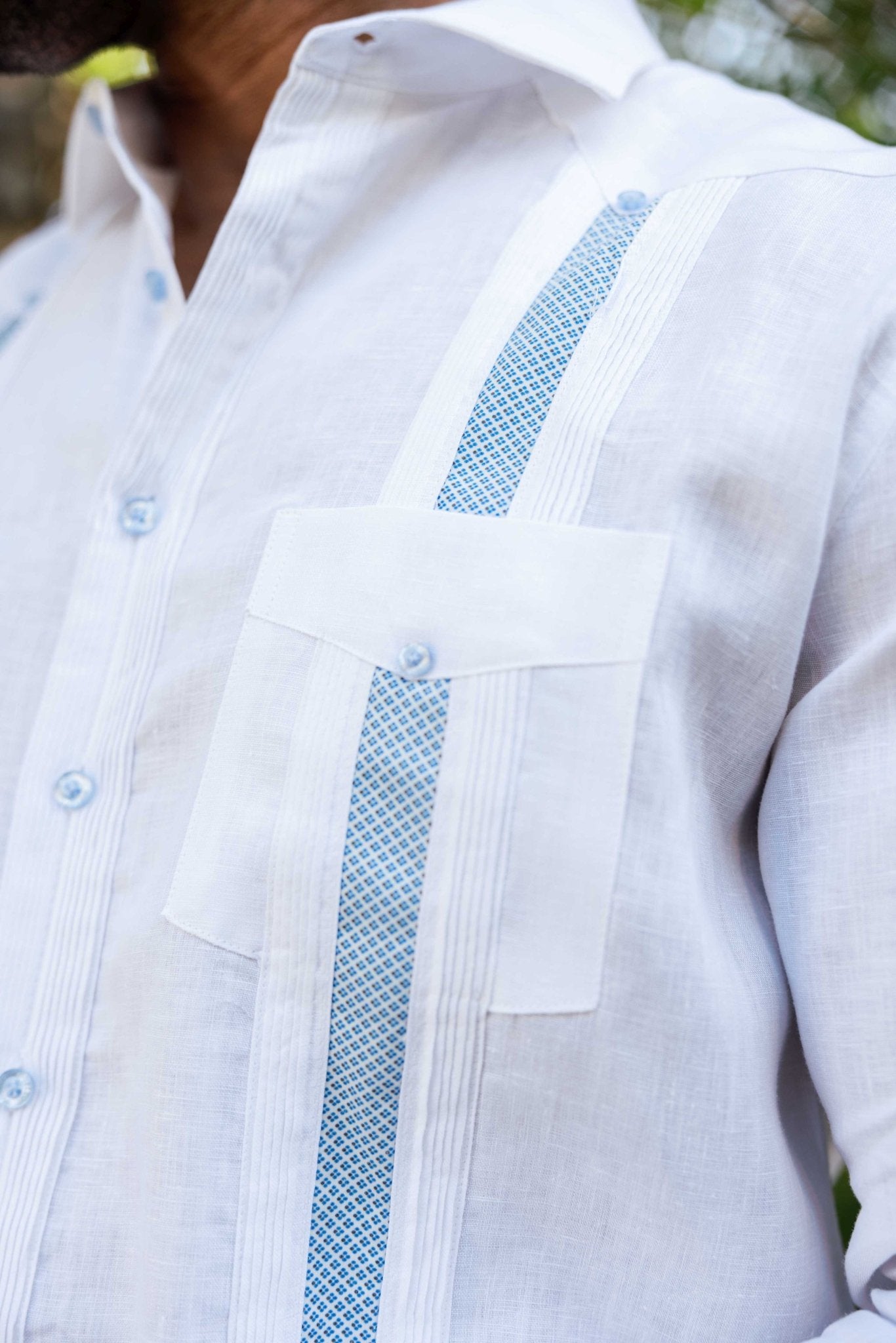 Close-up of white linen Men's Guayabera Shirt, showing blue artisan embroidery detail and pocket.