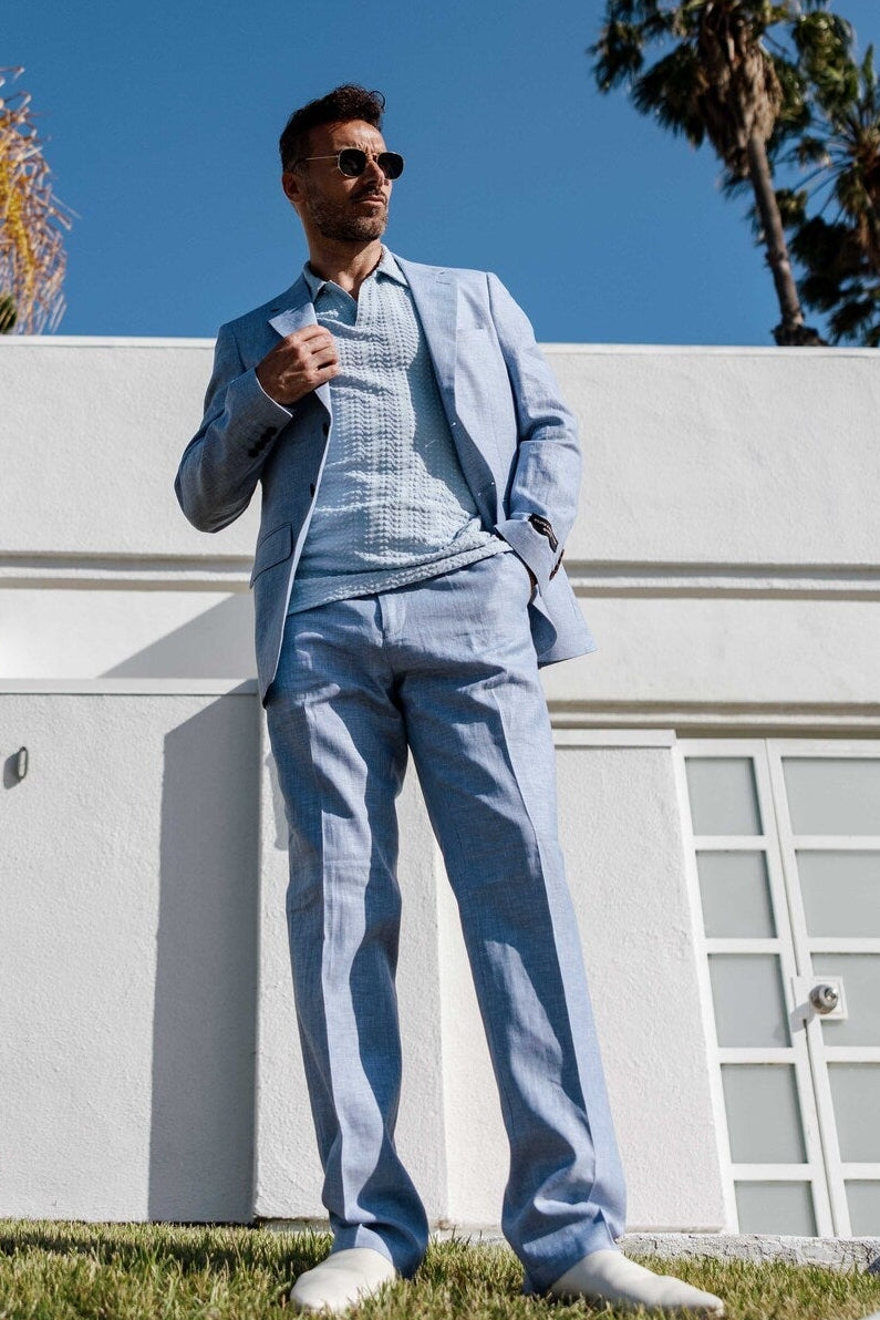 Man in a light blue suit standing in front of a white building with palm trees in the background