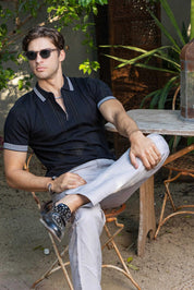 Man seated wears the black textured knit polo with stripe detail and light pants.