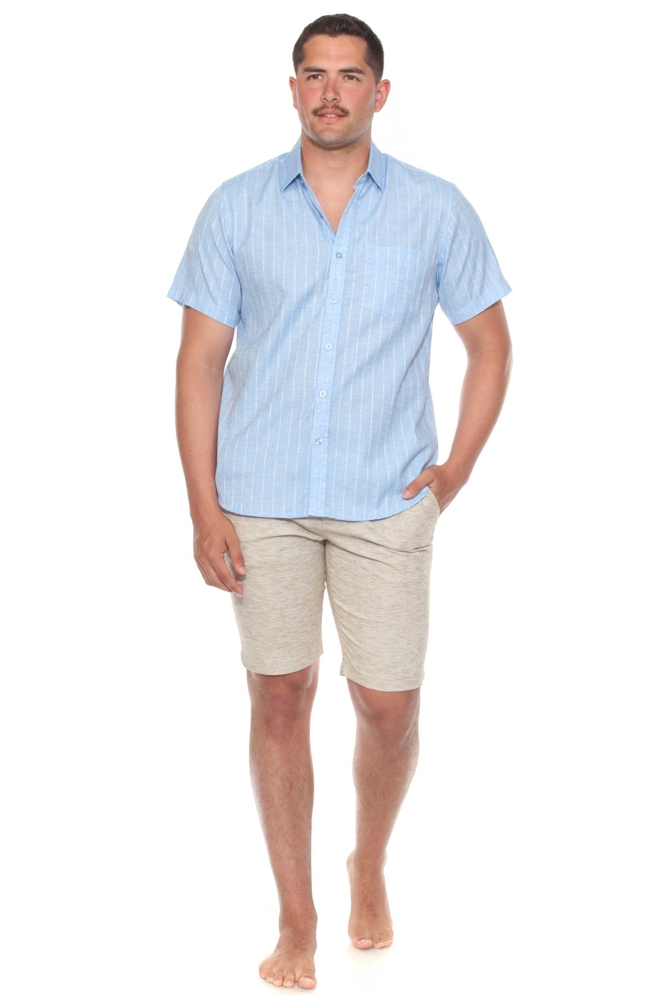 A man wearing a light blue Men’s Pinstripe Resort Shirt and beige shorts stands with one hand in his pocket.